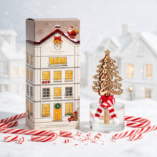 Reed diffuser Christmas Tree Peppermint Twist 6.9oz glass bottle with wooden tree topper beside a festive gift box.