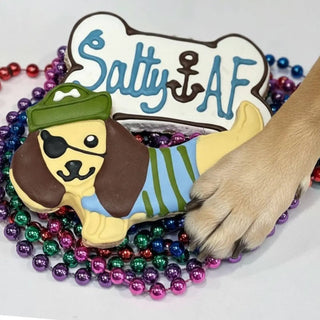 Pirate Salty AF Bone dog treat; bone-shaped cookie featuring pirate dog design and blue lettering, set among colorful beads.