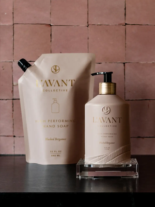 Two hand soap items: refill pouch and pump bottle in blush pink with gold accents and logo emblem