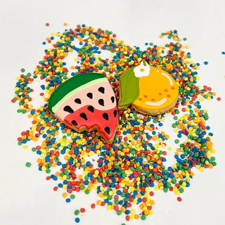 Watermelon slice cookies, 2 colorful pet biscuits with green rind, pink flesh and a yellow fruit-iced cookie on multicolor sprinkles.