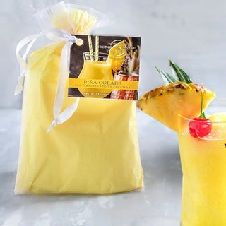 Pina Colada wine slushy mix bag in yellow packaging with white ribbon beside pineapple drink