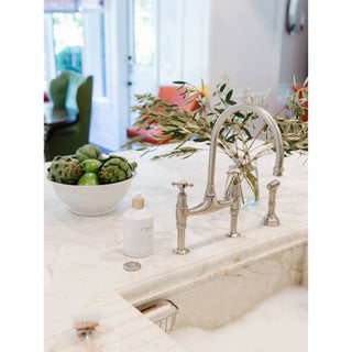 Fresh Linen High-Performing Dish Soap bottle with a gold pump beside a marble kitchen sink faucet.