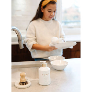 Fresh Linen Dish Soap bottle with beige pump on a kitchen counter, wooden brush and two white bowls.