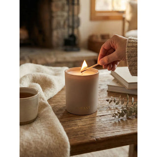 Candle Ambre Santal in beige ceramic jar, lit on a wooden table.