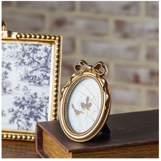 Antique gold oval frame with bow; two frames on a book, one with a bird illustration and the other with a toile scene.