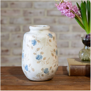 Blue flower bud vase, cream-glazed ceramic with blue floral pattern on a wooden table.