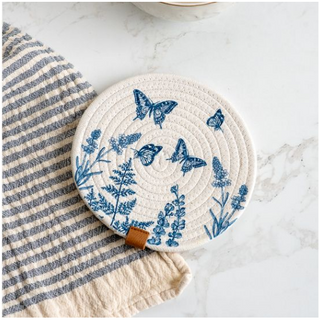 Butterfly round hot pad with blue butterfly motif on cream woven surface and a leather tab