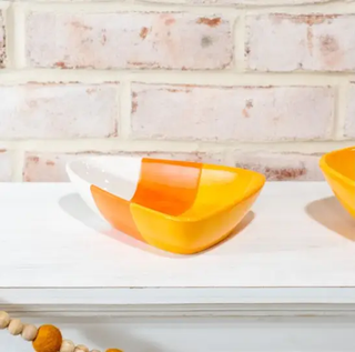 Two candy corn-themed ceramic dishes in white, orange, and yellow on a white shelf.