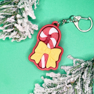 Keychain with candy cane and bow design on a green background with decorative branches.