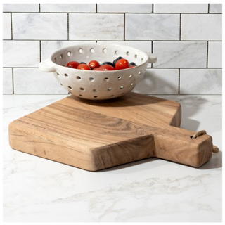 Chunky wood cutting board with a white perforated colander filled with cherry tomatoes