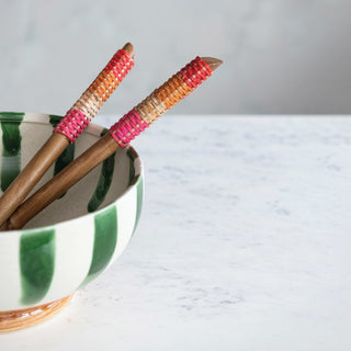 Salad servers set of 2 with rattan-wrapped handles in pink and orange, in a green-striped ceramic bowl.