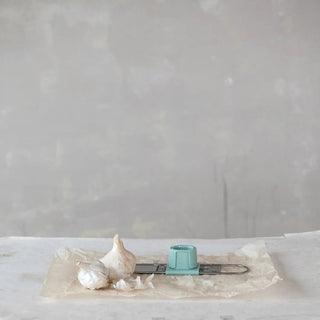 Stainless steel 3-way mini grater with teal adjustable mandolin slicer on parchment beside garlic