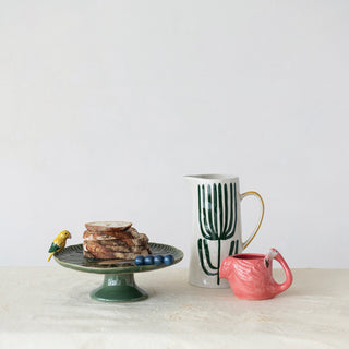 Flamingo-shaped mug, 14 oz stoneware in pink with white and brown accents; shown with a green pedestal plate