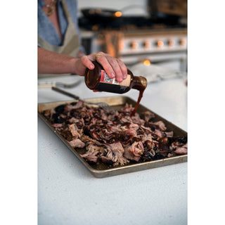 Chipotle BBQ Seasoning being poured over shredded pork on a baking sheet