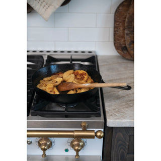 Bacon Apple Jam cooking in a cast-iron skillet on a gas stove with a wooden spoon