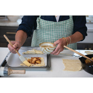 Bacon Apple Jam pastry filling on a dough sheet; baker in a green checked apron brushes dough.