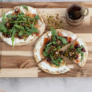 Cherry almond jam on rustic flatbreads with white cheese, arugula, and pistachios; jam jar in background.
