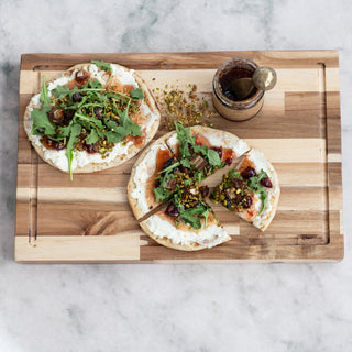 9 oz Cherry Almond Jam jar on a wooden cutting board beside arugula-topped flatbreads.
