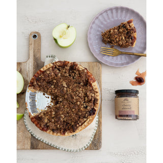 9 oz cherry almond jam jar next to a crumb-topped tart on a wooden board.