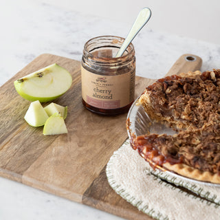Cherry almond jam jar, 9 oz, on a wooden board with sliced green apples and a crumb-topped pie