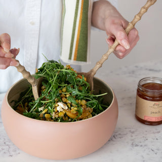 9 oz peach jam jar beside a pink bowl of greens and corn salad.