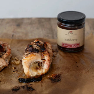 Cranberry chutney jar, 10 oz, amber glass with black lid, on parchment beside roasted chicken pieces.