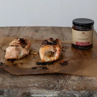 Cranberry chutney jar beside two roasted chicken pieces on parchment.