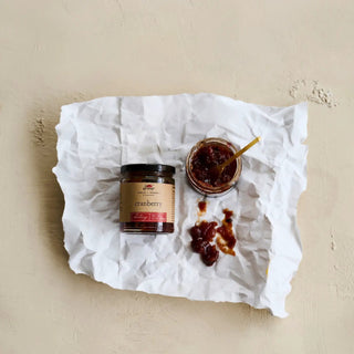 Cranberry chutney jar, 10 oz, glass with black lid and brown label on crumpled parchment, spoon in open jar.