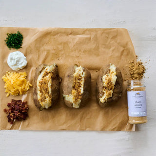 That's Amore Topper Seasoning, 3.3 oz jar, brown spice blend beside baked potatoes.