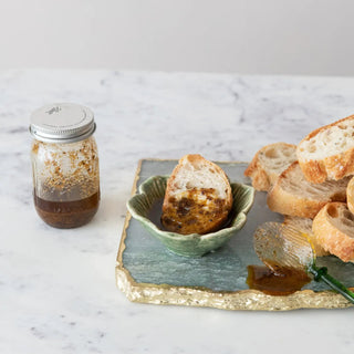 That's Amore Topper Seasoning in a glass jar with a metal lid, dark brown powder beside crusty bread slices.
