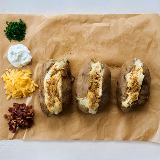 That's Amore Topper Seasoning on parchment with three loaded baked potatoes topped with sour cream, chives and cheese