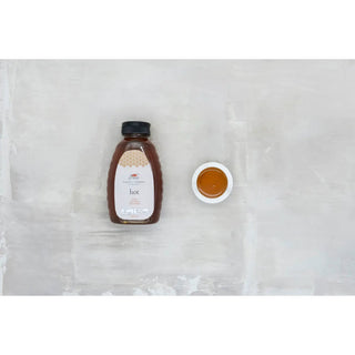 16 oz hot honey bottle in amber glass with black cap beside a small white dish of honey