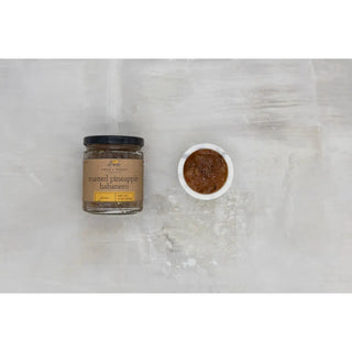 Roasted pineapple habanero jam jar, 9 oz, with brown kraft label and black lid, beside a small white dish of jam