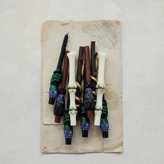 Unscented finger bone-shaped taper candles in white, brown and black, bundled on a board.