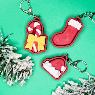 Three Christmas-themed keychains on a green background with decorative elements.