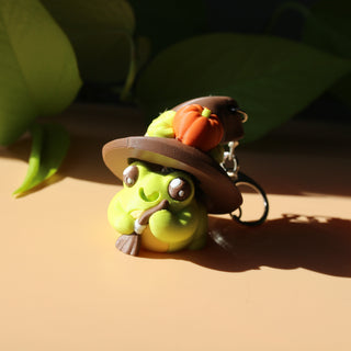 Green character keychain with a hat and carrot on a beige surface with green leaves in the background