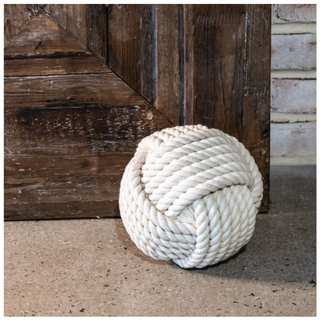 Nautical rope ball doorstop, white braided rope, resting against a rustic wooden door.