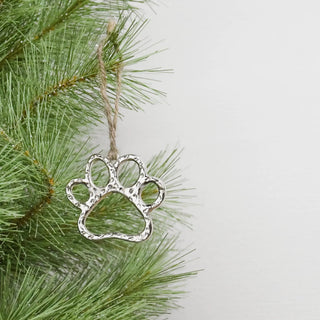 Silver dog paw ornament hanging from twine on pine branch