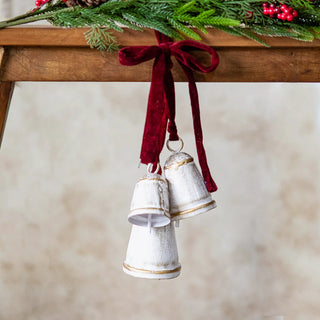 Two white-and-gold conical bells with red velvet ribbons, hanging from a wooden mantle.