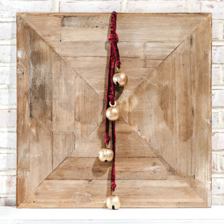 Gold bells on red velvet rope hanging against a rustic wooden backdrop