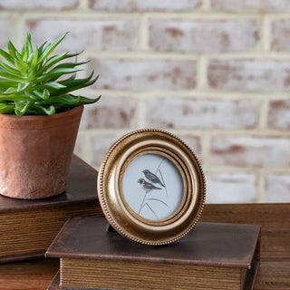 Vintage edge gold photo frame, round with beaded rim; placed beside a terracotta pot and two stacked books.