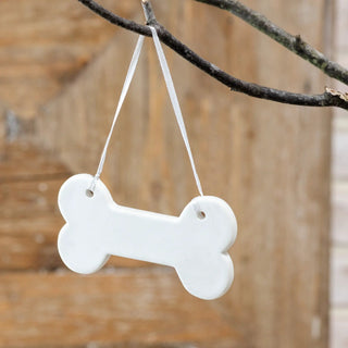 Two dog bone-shaped stoneware ornaments, white, hanging from white ribbons