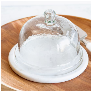 Round glass cake cover with white marble base on a wooden serving board