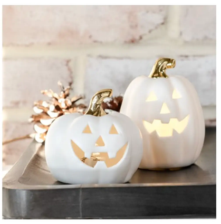 LED mini jack-o-lanterns: two white ceramic pumpkins with gold stems, carved faces lit from inside on a tray.