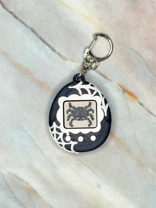 Black and white keychain with a spider design on a marble surface