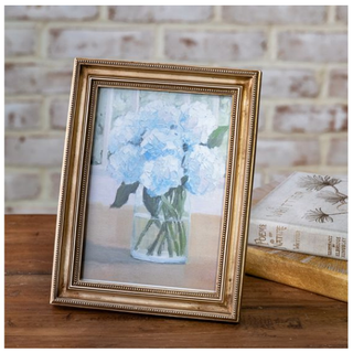 Vintage gold-edge photo frame displaying a blue hydrangea bouquet in a vase.