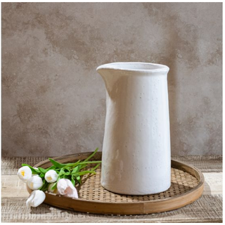 White ceramic pourer vase on a round wooden tray with white flowers.