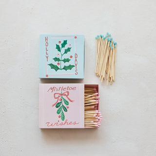 Two embossed safety matchboxes with holly and mistletoe botanicals; matches with blue and pink tips.