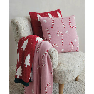 18-inch square cotton knit pillow in red and natural with tree and heart pattern, shown on a beige textured chair.