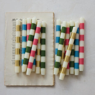 Taper candles, unscented striped in pink, blue, green and gold, arranged on an open book